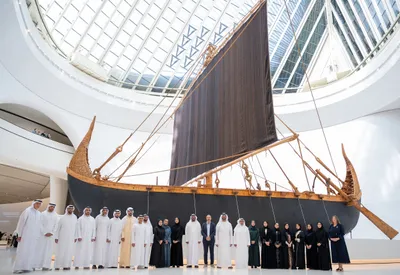 A traditional wooden dhow displayed indoors with a group of people standing in front