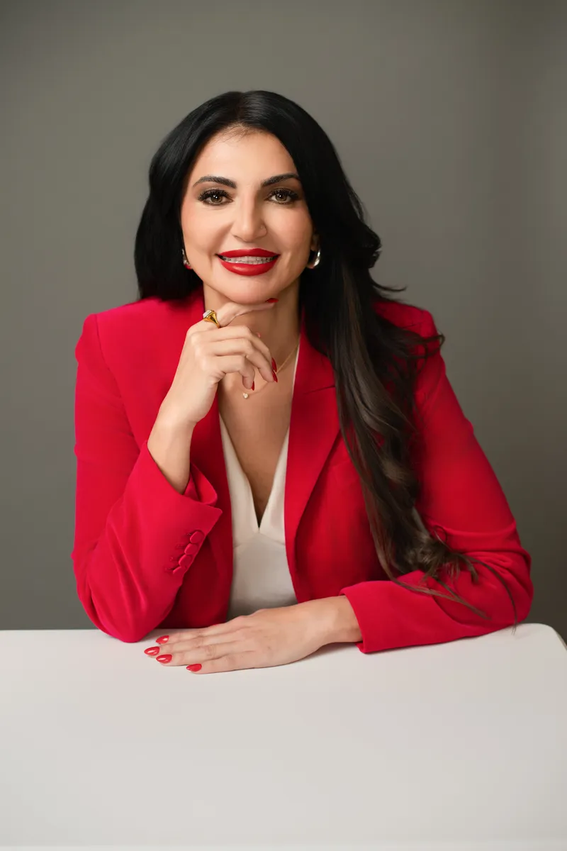Nicole Chaudry in a red blazer, smiling with her chin resting on her hand.