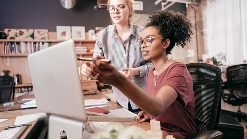 Two young women working together at a laptop in an office